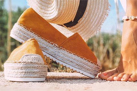 Een paar espadrilles met zomerse hoed en een blote voet