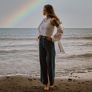 Model kijkend naar de zee met regenboog erboven