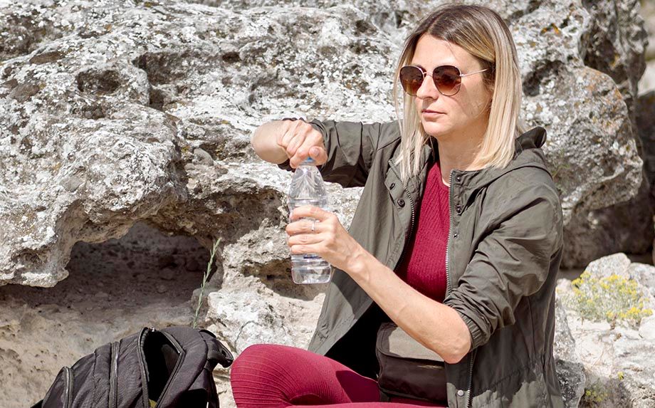 Zittende vrouw in outdoorkleding draait flesje water open